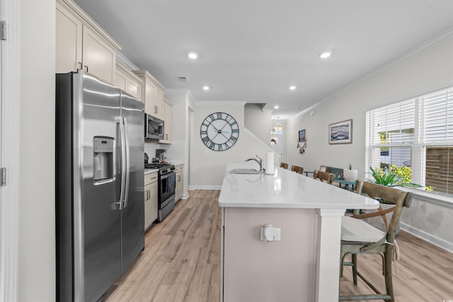 kitchen with an island with sink, light hardwood / wood-style flooring, stainless steel appliances, a breakfast bar, and crown molding