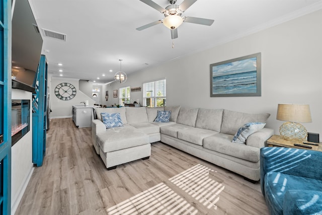 living room featuring ceiling fan with notable chandelier, light wood-type flooring, and ornamental molding