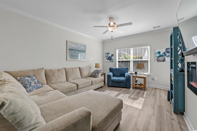 living room featuring light wood-type flooring, ceiling fan, a fireplace, and crown molding