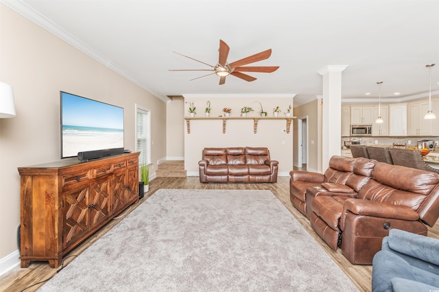 living room featuring decorative columns, ornamental molding, ceiling fan, and light hardwood / wood-style flooring