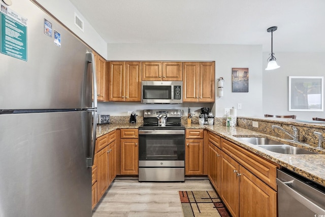 kitchen featuring appliances with stainless steel finishes, stone countertops, light wood-type flooring, decorative light fixtures, and sink