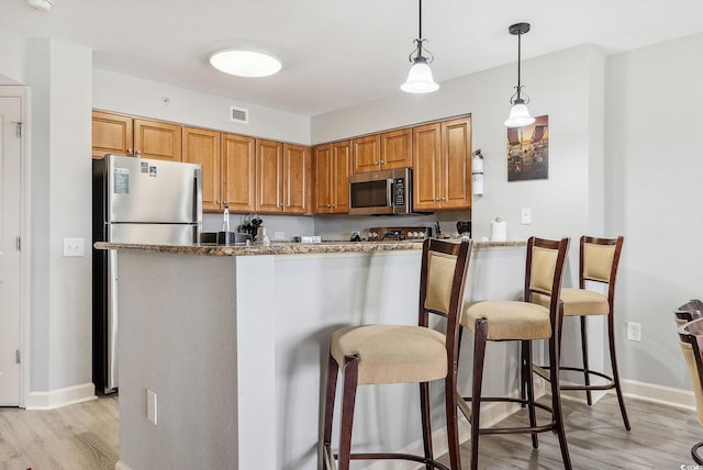 kitchen with pendant lighting, stone countertops, appliances with stainless steel finishes, a kitchen breakfast bar, and light wood-type flooring