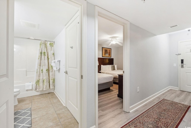 bathroom with hardwood / wood-style floors, ceiling fan, shower / tub combo, and toilet