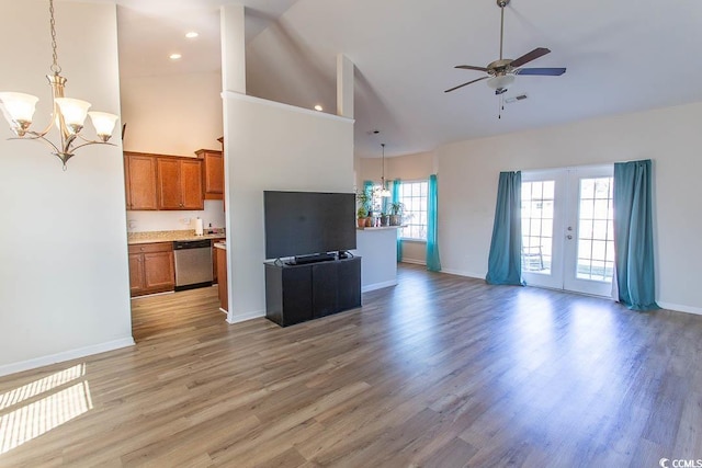 unfurnished living room featuring ceiling fan with notable chandelier, light wood-type flooring, high vaulted ceiling, and french doors