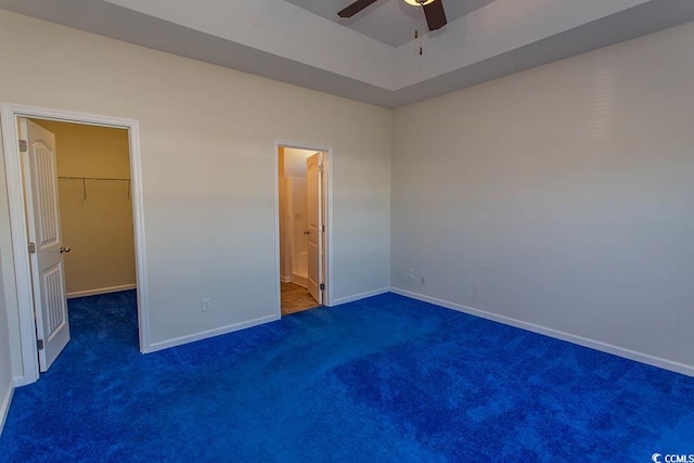 unfurnished bedroom featuring a walk in closet, ceiling fan, a closet, and dark carpet