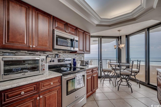 kitchen with light stone counters, tasteful backsplash, hanging light fixtures, stainless steel appliances, and ornamental molding