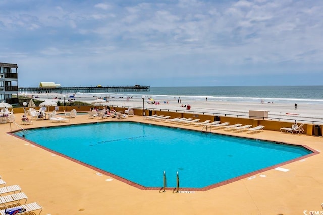 view of swimming pool featuring a view of the beach, a water view, and a patio area