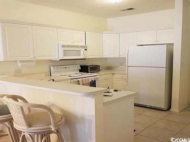 kitchen with white appliances, white cabinetry, a kitchen bar, and kitchen peninsula