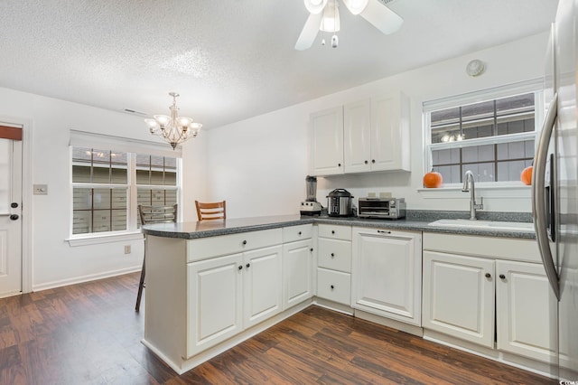 kitchen with white cabinets, sink, kitchen peninsula, ceiling fan with notable chandelier, and dark hardwood / wood-style flooring