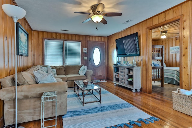 living room with ceiling fan, wooden walls, and wood-type flooring