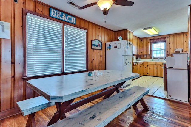 dining area featuring light hardwood / wood-style floors, wood walls, ceiling fan, ornamental molding, and sink