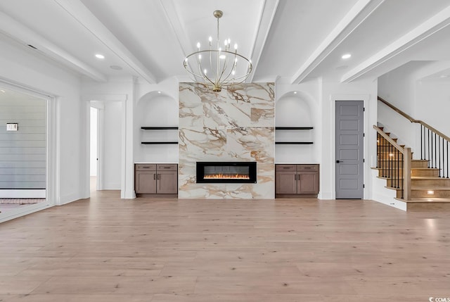 unfurnished living room featuring beam ceiling, light hardwood / wood-style flooring, a high end fireplace, built in features, and a notable chandelier