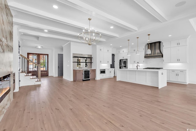 unfurnished living room featuring french doors, beam ceiling, light hardwood / wood-style flooring, a chandelier, and wine cooler