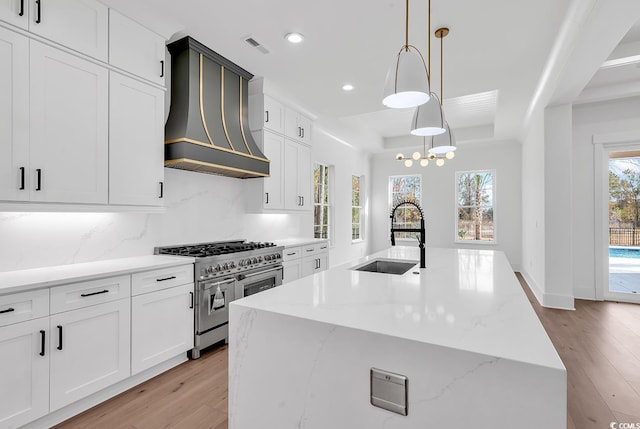 kitchen with custom exhaust hood, a large island with sink, range with two ovens, hanging light fixtures, and sink