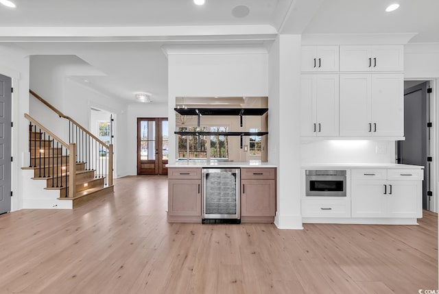 kitchen with white cabinets, light hardwood / wood-style floors, oven, and beverage cooler