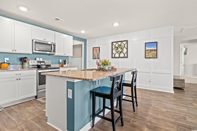 kitchen featuring stainless steel appliances, white cabinetry, and a center island with sink