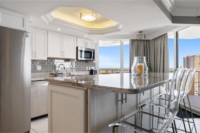 kitchen with white cabinetry, a breakfast bar area, a raised ceiling, and appliances with stainless steel finishes