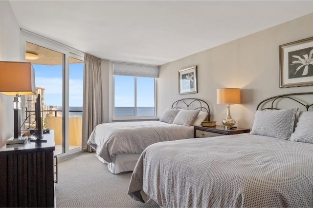 carpeted bedroom featuring expansive windows, a water view, and access to outside