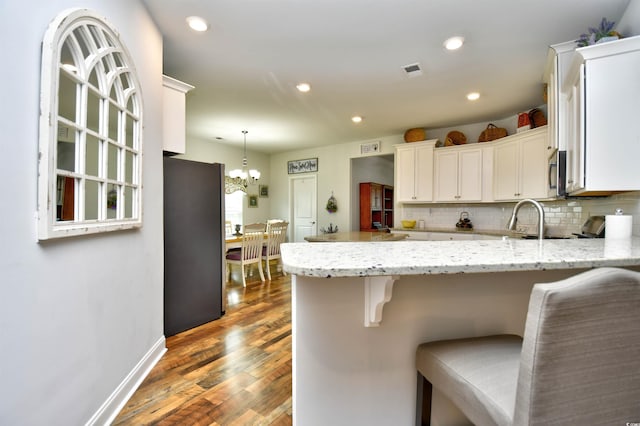 kitchen with kitchen peninsula, a kitchen breakfast bar, stainless steel appliances, and white cabinets