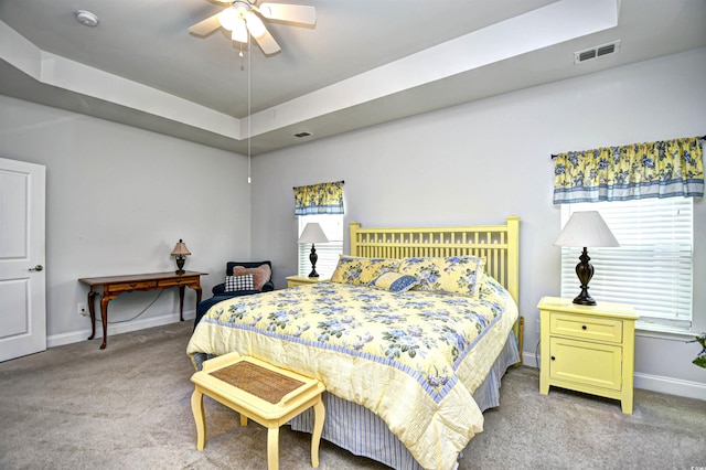 bedroom with light carpet, a tray ceiling, and ceiling fan