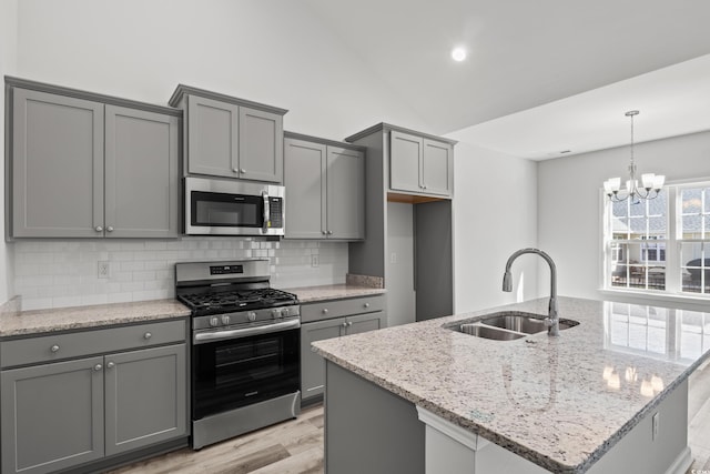 kitchen with appliances with stainless steel finishes, light stone countertops, sink, and gray cabinetry