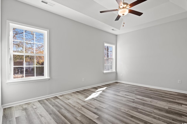 empty room featuring a raised ceiling, ceiling fan, and light hardwood / wood-style floors