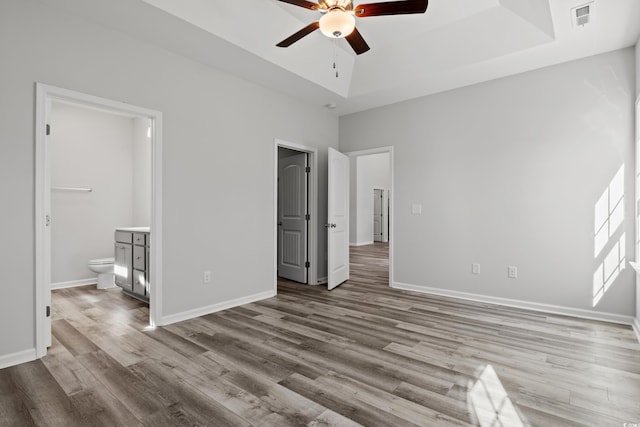 unfurnished bedroom featuring ceiling fan, connected bathroom, light hardwood / wood-style floors, and a tray ceiling