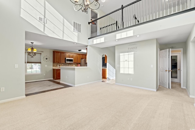 unfurnished living room featuring light colored carpet, an inviting chandelier, and a towering ceiling