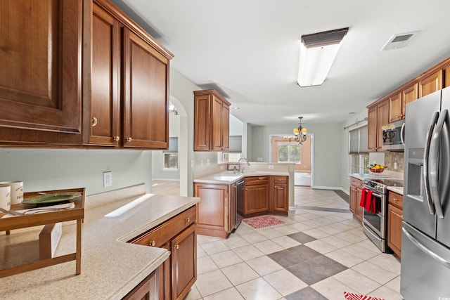 kitchen with kitchen peninsula, an inviting chandelier, appliances with stainless steel finishes, light tile patterned floors, and decorative light fixtures