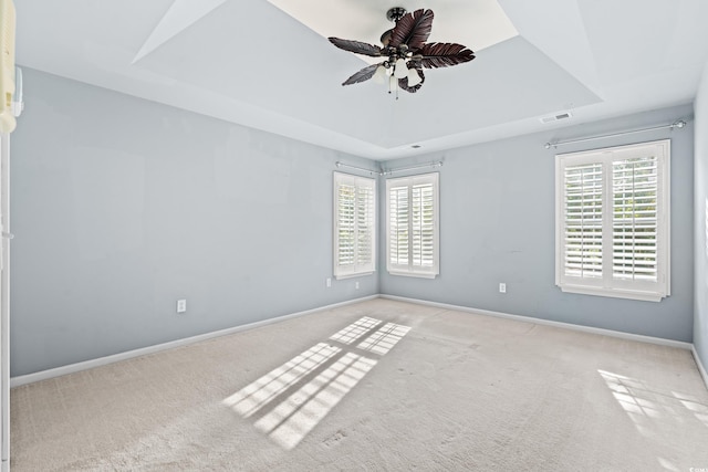 carpeted spare room with ceiling fan, a raised ceiling, and plenty of natural light