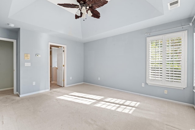 unfurnished bedroom featuring a tray ceiling, ensuite bath, ceiling fan, and light colored carpet