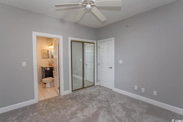 unfurnished bedroom featuring a closet, ensuite bathroom, light colored carpet, and ceiling fan