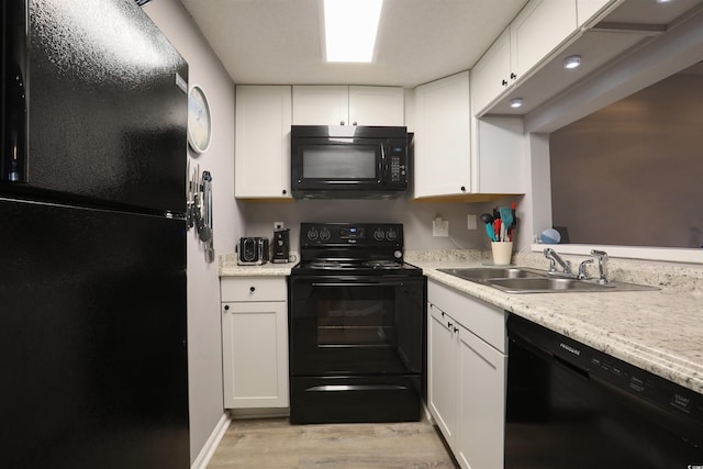 kitchen with light hardwood / wood-style floors, white cabinets, light stone countertops, black appliances, and sink