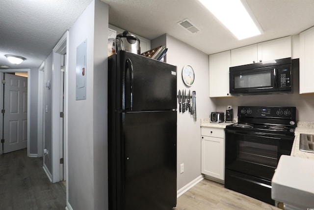 kitchen featuring white cabinets, electric panel, a textured ceiling, black appliances, and light wood-type flooring