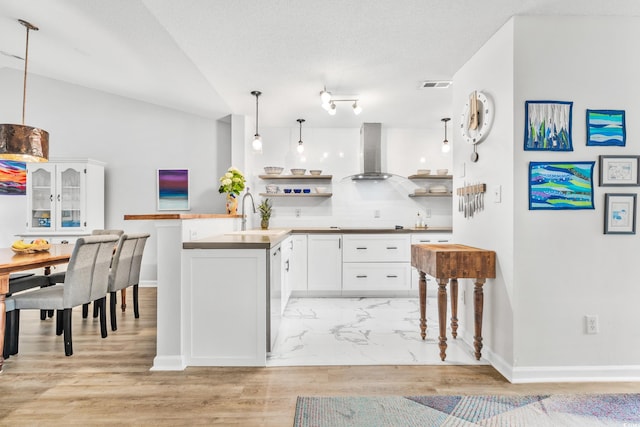 kitchen with pendant lighting, lofted ceiling, white cabinets, and wall chimney range hood