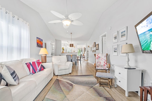 living room with light wood-type flooring, vaulted ceiling, ceiling fan, and a wealth of natural light