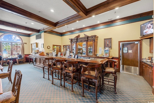 dining space featuring beamed ceiling, a textured ceiling, indoor bar, carpet, and ornamental molding