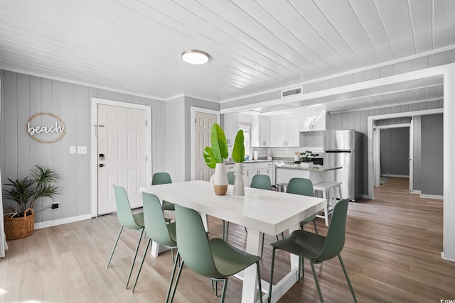 dining space featuring ornamental molding, wooden walls, and light hardwood / wood-style floors