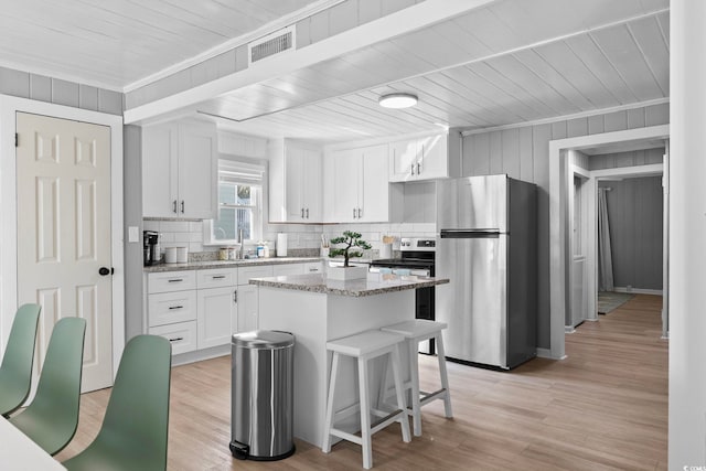 kitchen featuring white cabinetry, appliances with stainless steel finishes, light stone counters, and a center island