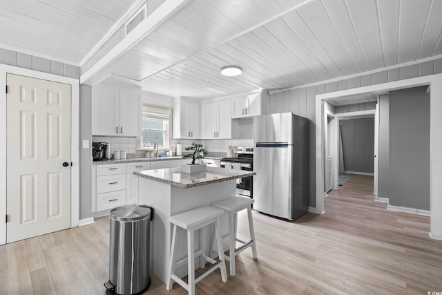 kitchen with light stone counters, white cabinets, stainless steel appliances, and a kitchen island