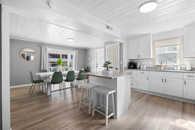 kitchen with light stone counters, light wood-type flooring, white cabinetry, and a healthy amount of sunlight