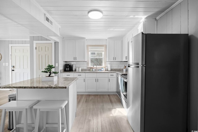 kitchen with light stone counters, sink, light hardwood / wood-style flooring, white cabinetry, and appliances with stainless steel finishes