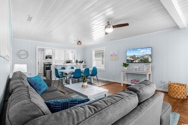 living room with light hardwood / wood-style floors, wood walls, ceiling fan, and beamed ceiling