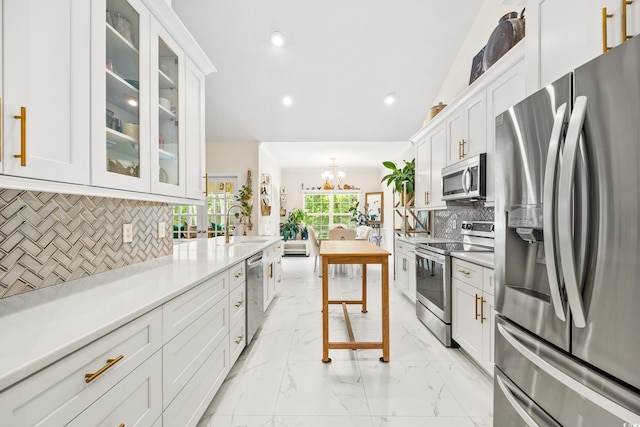 kitchen featuring white cabinets, decorative light fixtures, stainless steel appliances, an inviting chandelier, and decorative backsplash