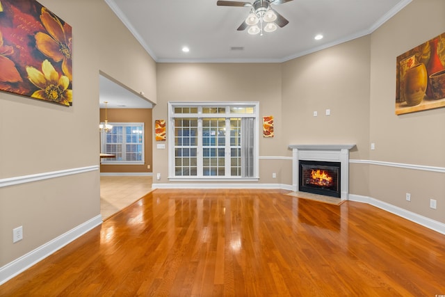 unfurnished living room featuring ceiling fan with notable chandelier, light hardwood / wood-style flooring, and crown molding