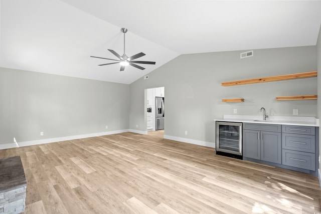 bar featuring sink, stainless steel refrigerator with ice dispenser, gray cabinets, light wood-type flooring, and beverage cooler