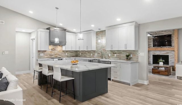 kitchen featuring lofted ceiling, hanging light fixtures, light stone countertops, a kitchen island, and white cabinetry