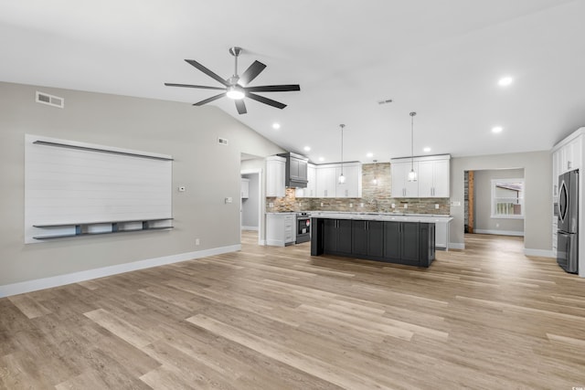 kitchen with a center island, vaulted ceiling, appliances with stainless steel finishes, decorative light fixtures, and white cabinetry