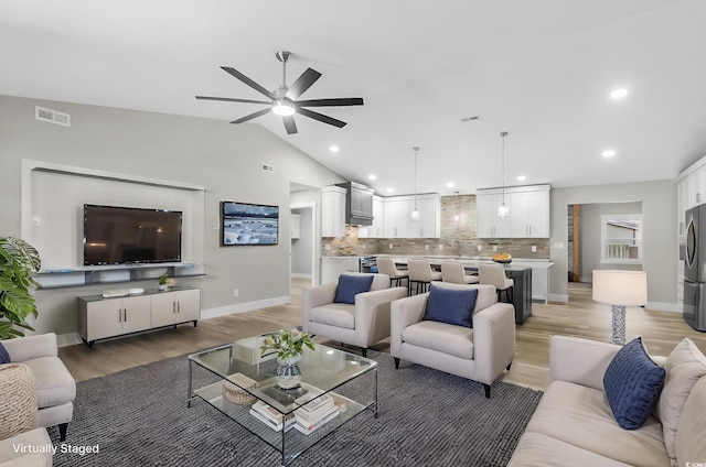 living room featuring light wood-type flooring, ceiling fan, lofted ceiling, and sink