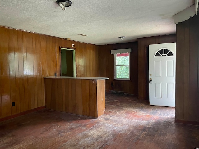 kitchen featuring a textured ceiling, kitchen peninsula, wood walls, and dark wood-type flooring